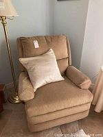 Brown upholstered reclining arm chair with beige decorative pillow on the seat, viewed from the front.