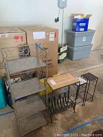 Four-tier metal shelf, metal magazine table stand, and three small metal plant stands grouped on garage floor with boxes behind