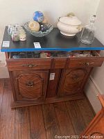 Side view of wood look veneer side table with black matte top surface. Drawer open showing contents inside drawer. Two double door cabinet below with handles and wood paneling detail.