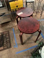 Two round wooden accent tables with dark walnut finish, placed side by side on a concrete floor with other furniture around.