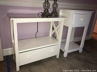 Two white laminated tables side by side on carpet. Side table has open shelf, end table has drawer and curved legs.