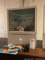 Lighted beige wooden display cabinet with glass front and drawer, situated on a table in a basement.