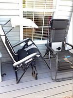 Two black anti-gravity lounge chairs side by side on a porch. One chair has a white sunshade canopy attached, the other does not. Both have black mesh fabric and metal frames with elastic cord suspension.