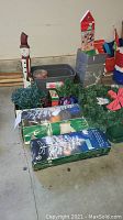 Photo showing assorted Christmas decorations including wooden snowman figure, string lights, greenery wreaths, and boxed light display items.