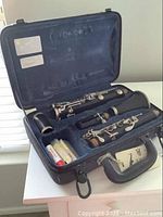 Open clarinet case showing disassembled clarinet parts including mouthpiece and reeds.