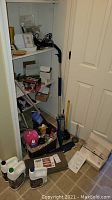 Photo showing Bona floor cleaners, cleaning fluids in basket, plungers, Swiffer Wet Jet mop, unopened boxes, and stair treads against closet wall.