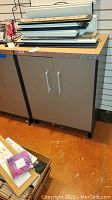 Front view of gray Coleman cabinet with diamond plate edge on top and two doors with silver handles, scratches visible on cabinet surface.