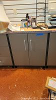 Front view of gray Coleman metal storage cabinet with diamond plate top trim and two silver vertical handles. Visible scratches and surrounding items show condition.