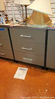 Three photos of Coleman steel cabinet with model number 40452 on paper in front. Each photo shows the cabinet's full front view with three drawers and various lamps on top. Scratches and wear visible.