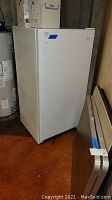 Side view of white Kenmore upright freezer, showing handle on the side and some wear marks.