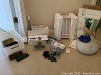Photo of health aids including blood pressure monitors, light therapy lamp, vaporizer, eyeglasses with cases, and small accessories arranged on the floor near white basket