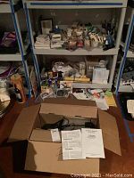 Full shelf and floor contents including the projector box, art supplies, paints, stamps, ribbons, canvases, and miscellaneous craft materials
