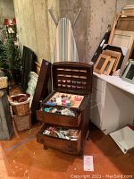 Full view of vintage wooden sewing box opened, showing thread spools and drawers with sewing accessories, with striped ironing board behind