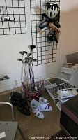 Photo showing rollerblades, ski boots, and golf club set in an upright container against a garage wall