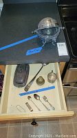 Drawer containing several pieces of flatware, silver plated bell, brass bell, and two Gorham rings visible in a upper shot