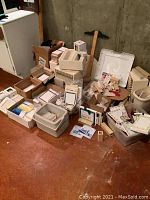 Overall view of assorted ceramic tiles, stacking racks and art supplies collected on floor in basement with concrete wall background.