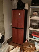 Full view of the closed cabinet in a basement, showing the wood-look double door design and black trim with surrounding basement items, indicating size and condition.