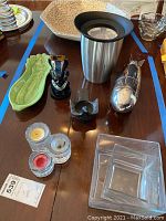 Photo shows various barware and decorative items on a wooden table including a mosaic bowl, celery-shaped tray, champagne cooler, candle holders, and square glass containers.