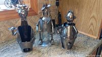 Three metal wine bottle holders on a kitchen counter, showing full figures and details.