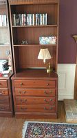 Full view of wooden file cabinet with two large drawers and matching hutch above with shelves, holding books and lamp (contents not included).