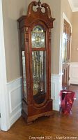 Full front view of walnut-tone wooden case with glass door showing weights and pendulum