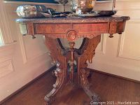 Full side view of the marble top table showing the carved wooden base and marble surface with items on top.