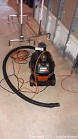 Front view of Ridgid portable shop vacuum showing hose and orange power cord on concrete floor.