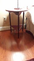 Full view of the wooden side table on a hardwood floor showing four turned legs and a triangular lower shelf.