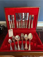 Inside of flatware case showing the knives at top and spoons, forks on bottom with red velvet interior
