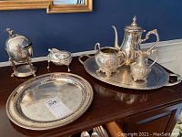 Full view of all items including tea set pieces on serving tray, poached egg server with eagle finial, covered chafing dish and large serving tray.