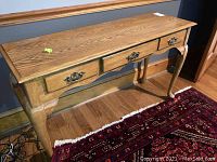 Front angle view of wood sofa table showing three drawers with metal handles and carved legs.