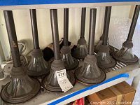 Nine solar outdoor garden lights with metal stakes and conical glass lampshades, dusty and in storage on a shelf.
