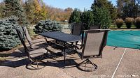 Wide shot of outdoor patio table and five swivel chairs beside a pool and patio area.