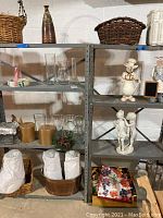 Shelf display showing glass vases, pillar candles, woven baskets, a wooden ice bucket, and a white garden statue of cherubs.
