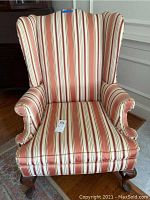 Front view of the wing back chair showing striped cloth upholstery in red, white, and beige with rolled arms and wooden legs.