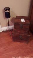 Wider view showing wooden boxes stacked beside iron candle holder with pillar candle on wooden floor near wall.
