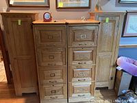 Two matching wood four-tier cabinets side by side with drawer-front style vertical panels, metal pull handles on middle sections, and single doors on the sides with round knobs.