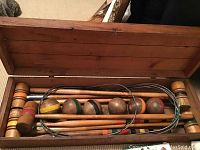 Opened wooden box containing multiple wooden croquet mallets, wooden balls, and metal hoops inside