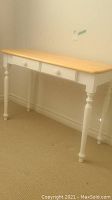 Full front view of wood desk showing natural wood top and painted white base with two drawers and turned legs.