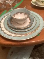 Stacked place setting showing dinner plate, luncheon plate, bread plate, teacup and saucer with light blue border and gold leaf motif
