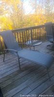 Photo of outdoor mesh sun lounger with reclined backrest and extended seat, metal frame, located on a wooden deck with trees in the background.