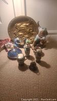 Collection of Asian themed items arranged on carpet, includes mud men figurines, salt and pepper shakers, bell, miniature plate and brass decorative plate.