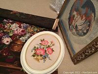 Three needlepoint artworks: largest framed square bird needlepoint, oval floral needlepoint in white frame, and unframed floral piece.