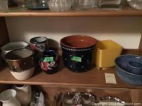 Wide view of six ceramic planters, vases and pottery bundt pan on wooden shelf.