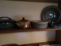 Overview of five pottery pieces on wooden shelf: two lidded dishes and three bowls