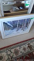 Framed print leaning against mirror showing metal frame and carpet background.
