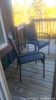 Two black resin wicker chairs placed on a wooden deck near a railing and house wall.
