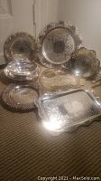 Overview of all eight silver plated plates, bowls, and platter showing reflective silver surfaces and detailed engraved patterns and pierced edges.