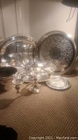 Group of 6 silver plated serving pieces including trays, candle holder, and plates displayed on carpeted floor.
