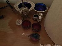 Photo showing two cobalt blue glass bowls with silver plate edges, silver mate holder with straw, cranberry glass salt cellars, silver salt and pepper shakers, and red/blue art glass bird paperweight
